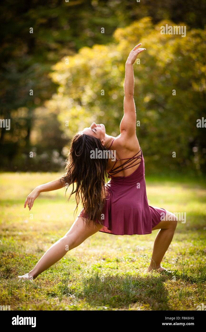 Full length rear view of mid adult woman wearing short dress dancing on grass, head back arm raised Stock Photo