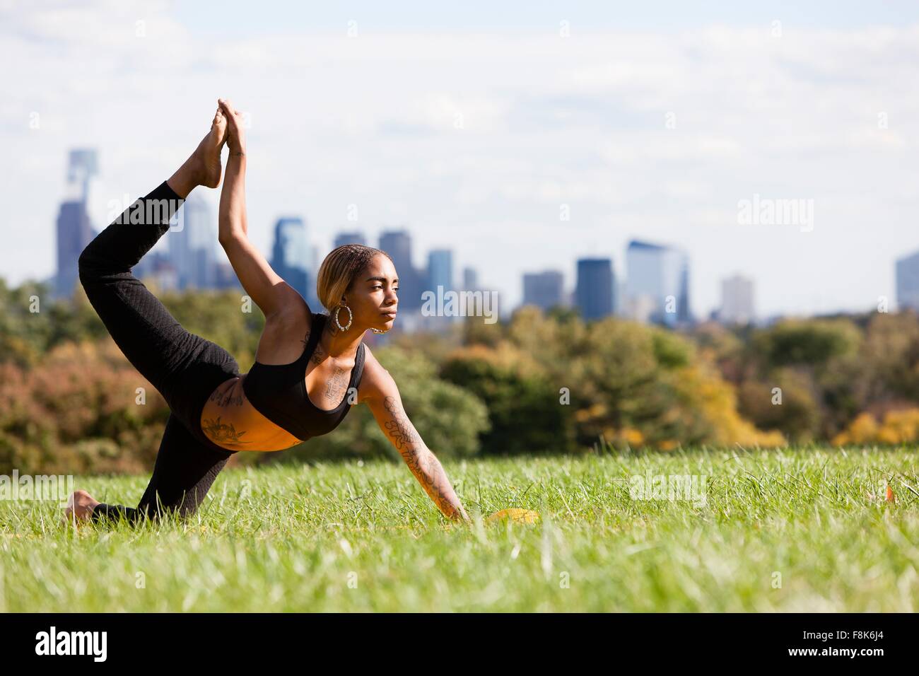 Side view of young woman on grass in yoga position, leg raised, looking ...