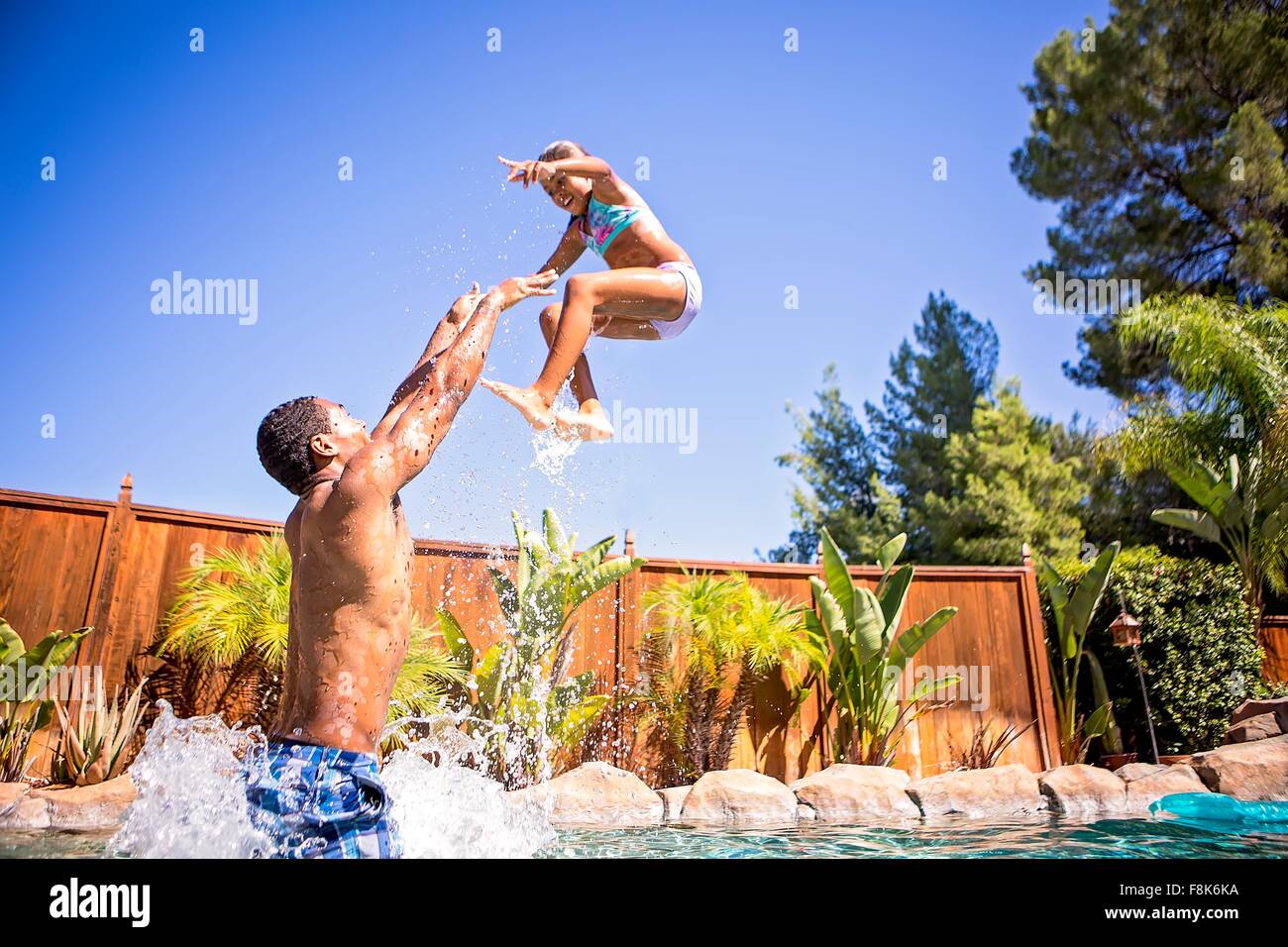 Side view of father in swimming pool throwing daughter in air smiling