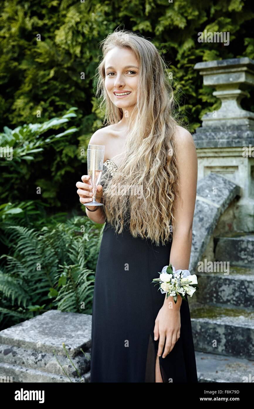 Teenage girl wearing prom dress and corsage holding champagne flute looking at camera smiling Stock Photo