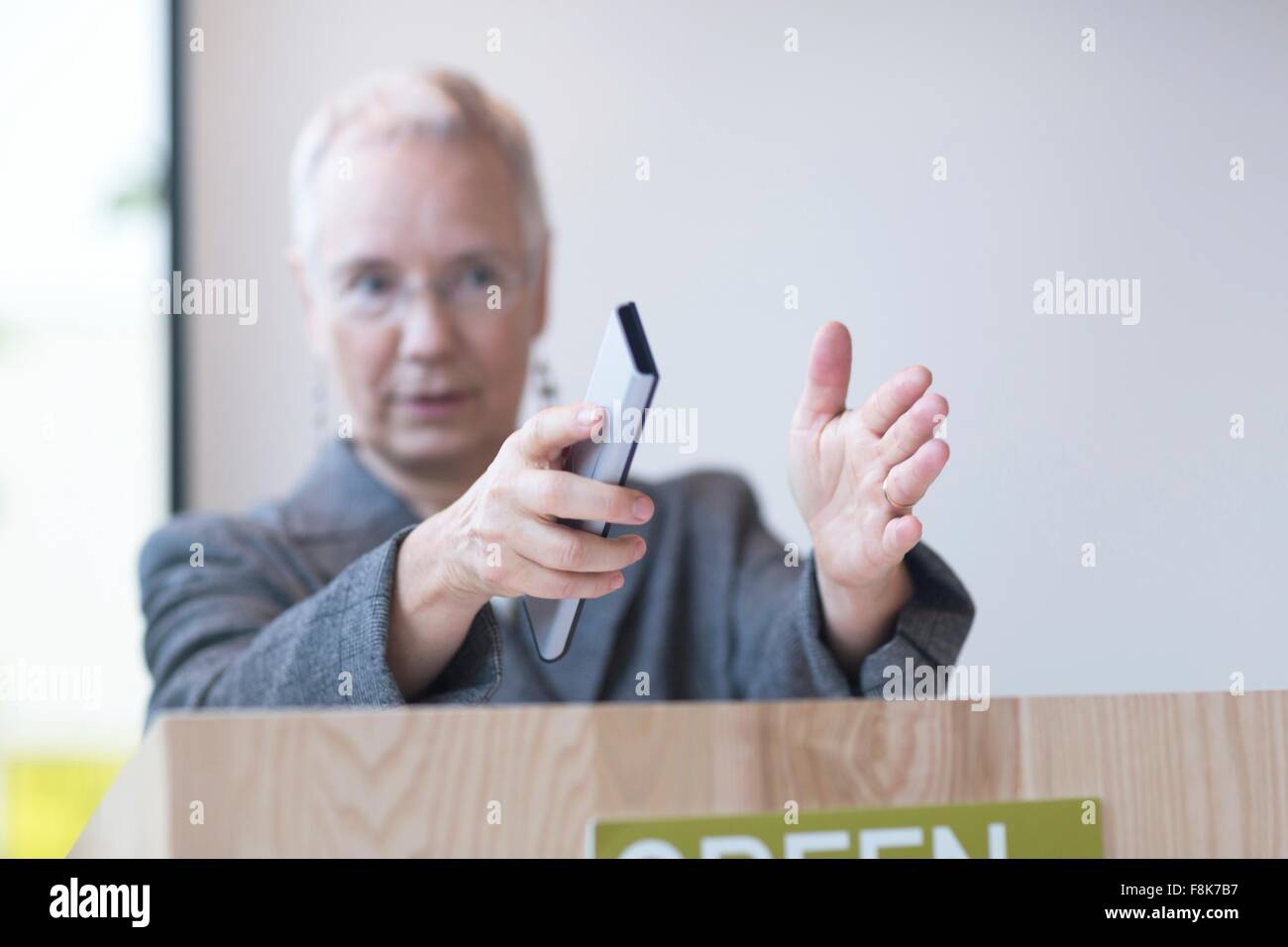 Mature woman behind podium giving lecture holding remote control, gesticulating Stock Photo