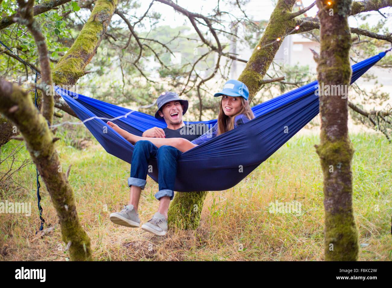 Happy adult couple reclining in blue hammock between trees Stock Photo