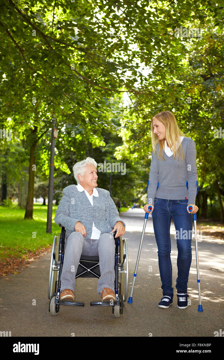 Two women in wheelchair and on crutches talking in a park Stock Photo -  Alamy