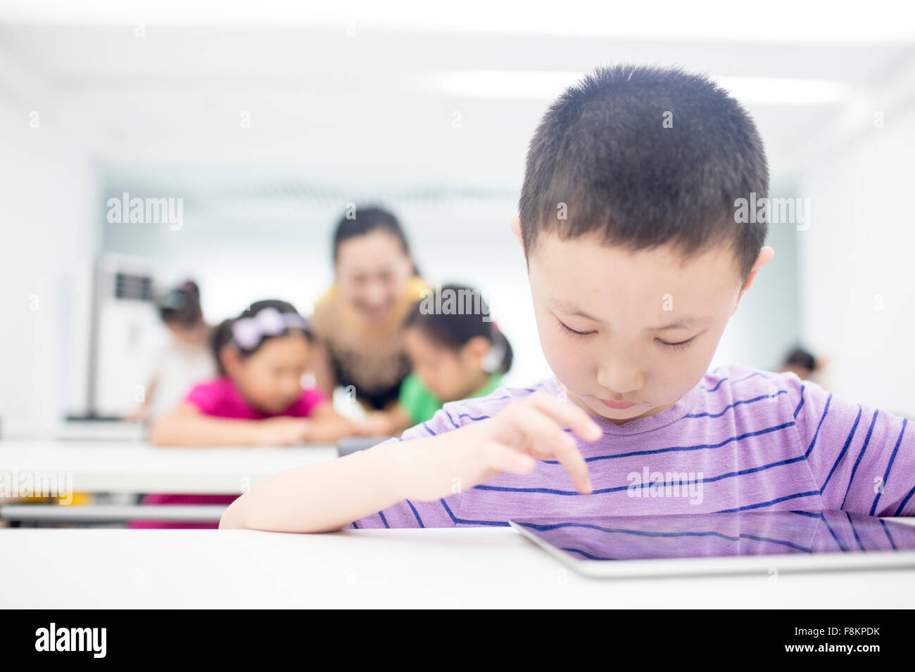 Boy using digital tablet while sitting at table in classroom Stock Photo