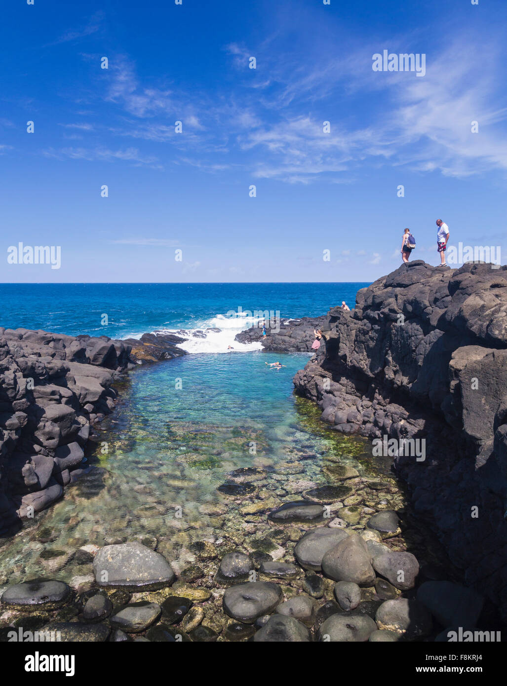 Tourists overlook snorkeling swimmers in the sea at Queens Bath tide