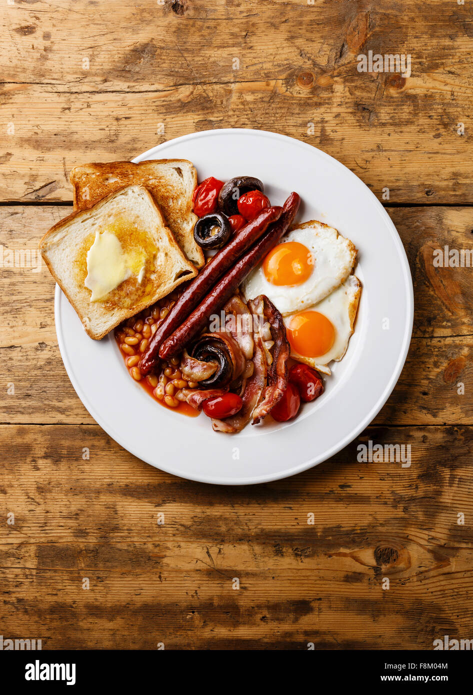Full English Breakfast with fried eggs, sausages, bacon, beans, toasts, tomatoes and mushrooms on wooden background Stock Photo