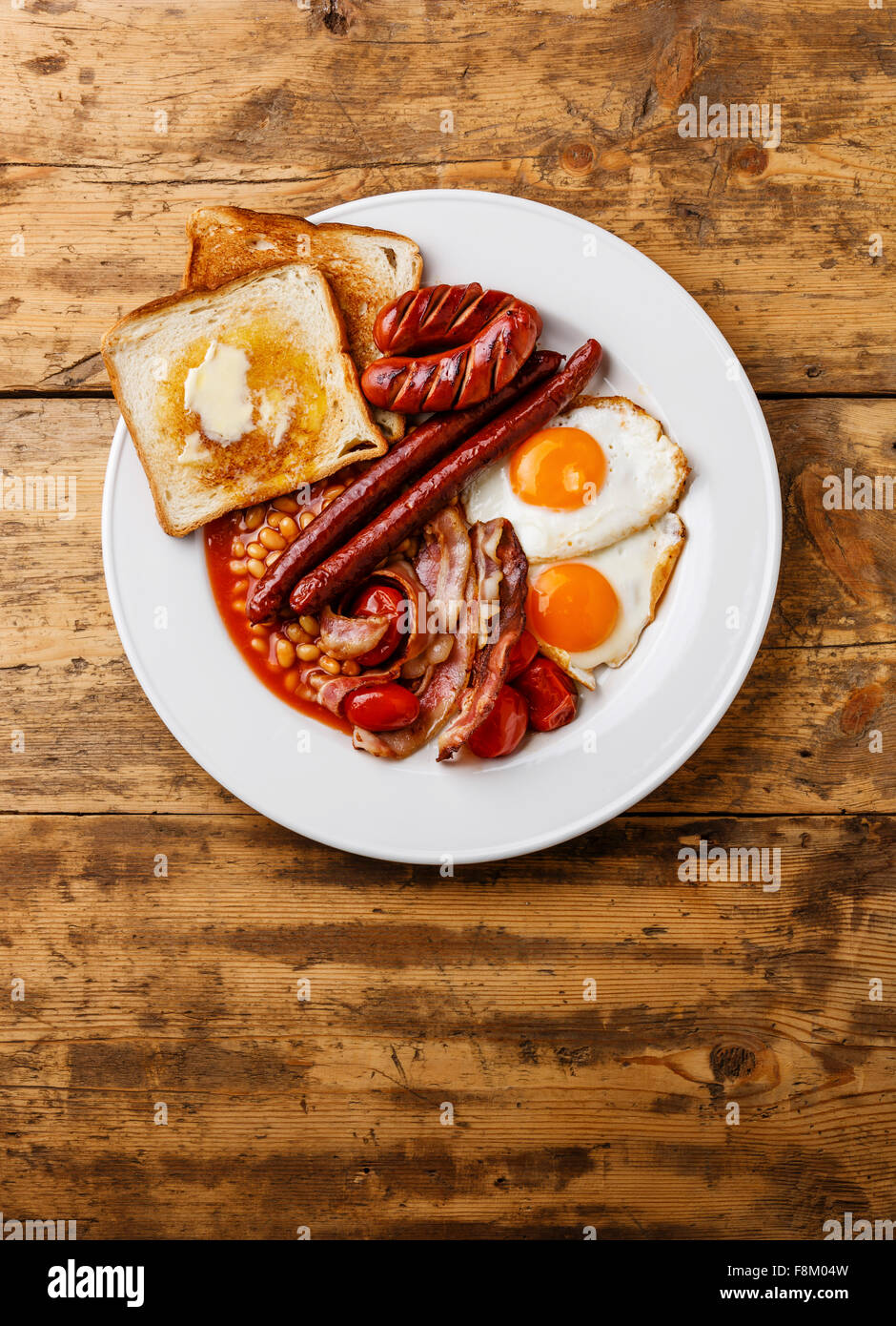 Full English Breakfast with fried eggs, sausages, bacon, beans, toasts, tomatoes and mushrooms on wooden background Stock Photo