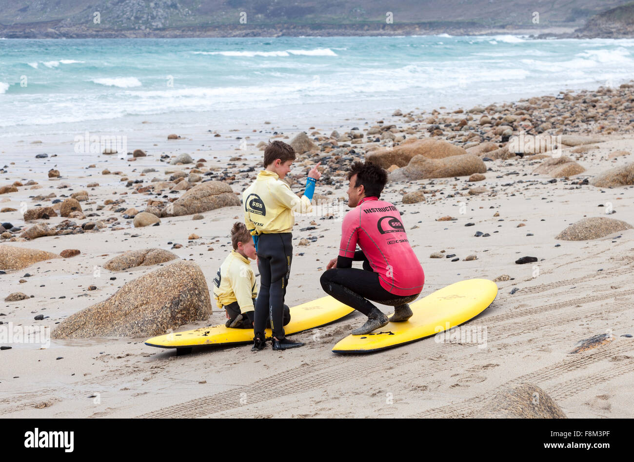 An instructor and two young male Surfers learning how to surf on surf boards on Sennen Cove