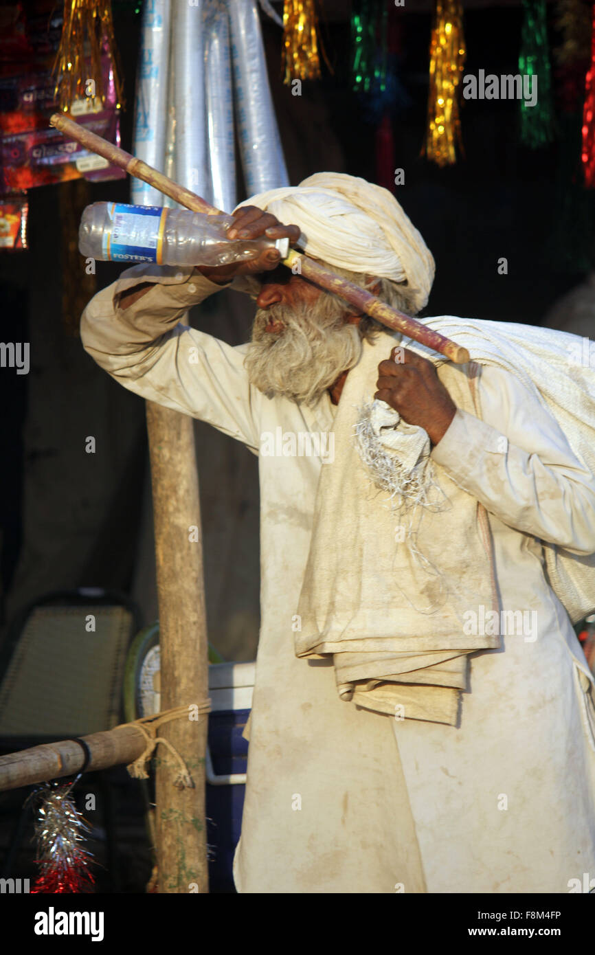 PUSHKAR, INDIA - NOV 28 2014: Indian senior man, white dressed, walking with a cane and a big sack on hos shoulder, at Pushkar F Stock Photo