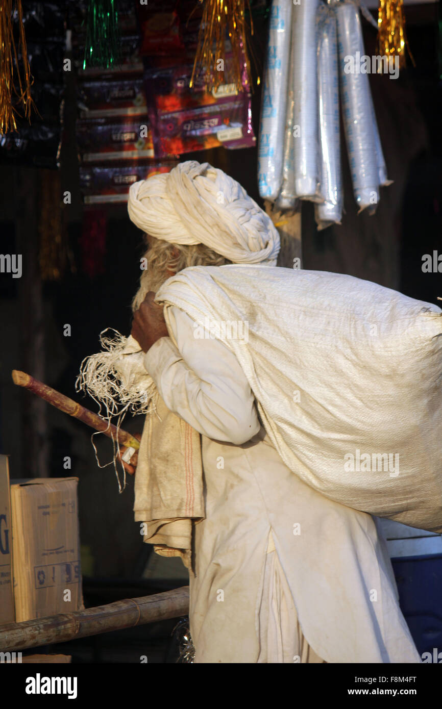 PUSHKAR, INDIA - NOV 28 2014: Indian senior man, white dressed, walking with a cane and a big sack on hos shoulder, at Pushkar F Stock Photo