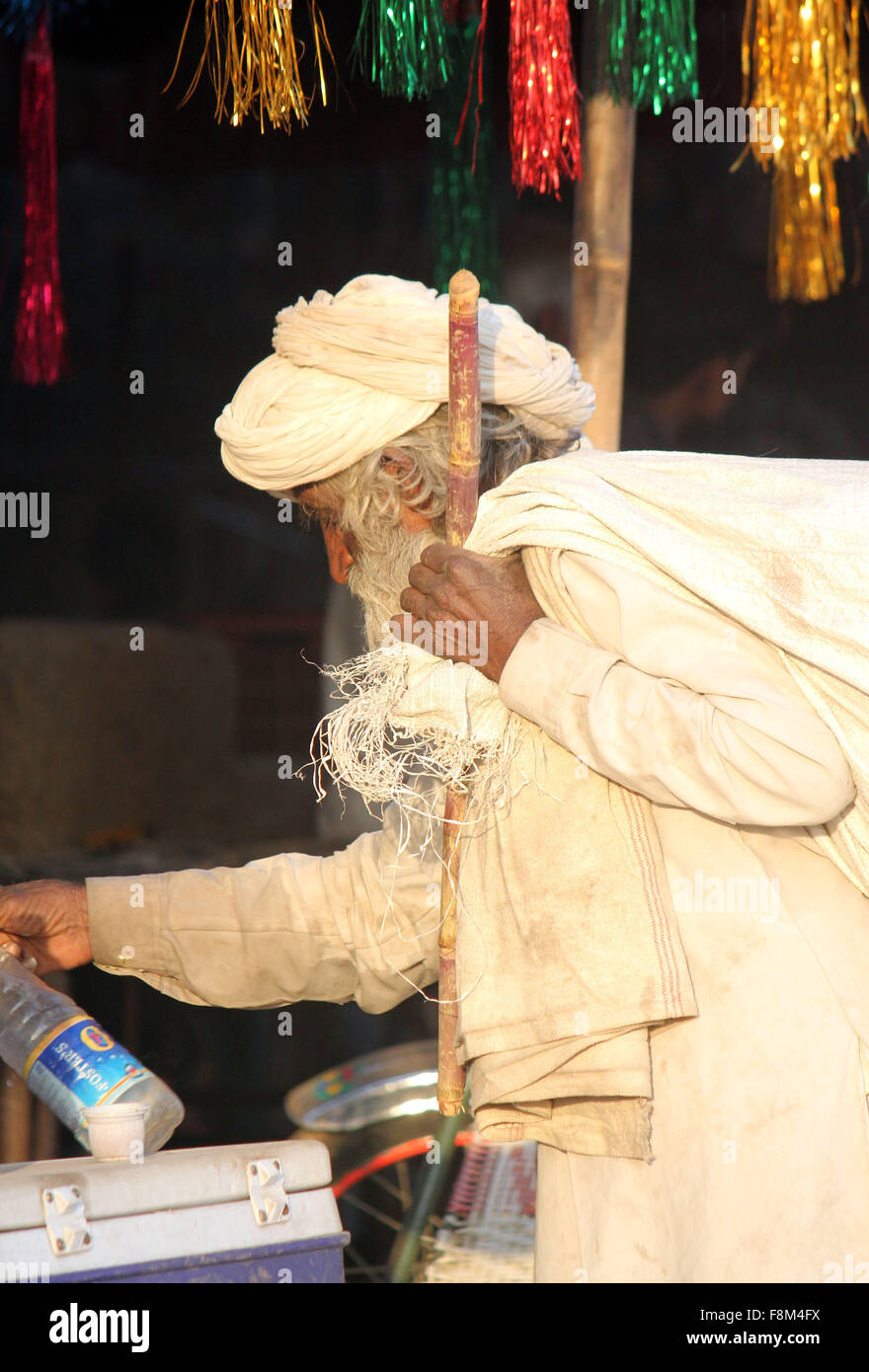 PUSHKAR, INDIA - NOV 28 2014: Indian senior man, white dressed, walking with a cane and a big sack on his shoulder, at Pushkar F Stock Photo