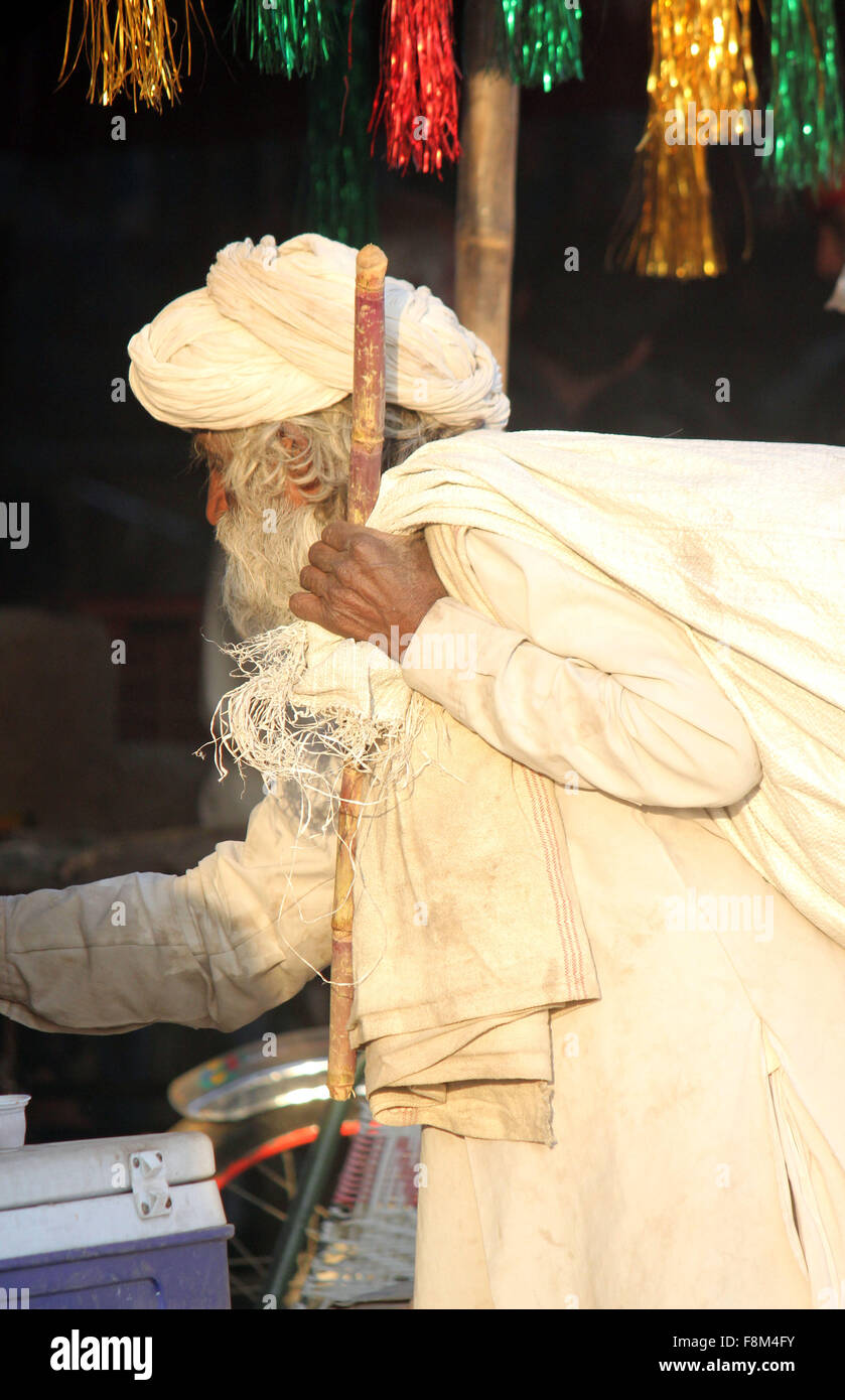 PUSHKAR, INDIA - NOV 28 2014: Indian senior man, white dressed, walking with a cane and a big sack on hos shoulder, at Pushkar F Stock Photo