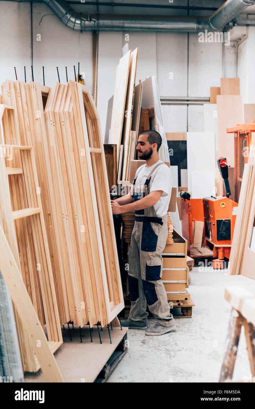 Young man in carpentry workshop stacking timber construction frames Stock Photo