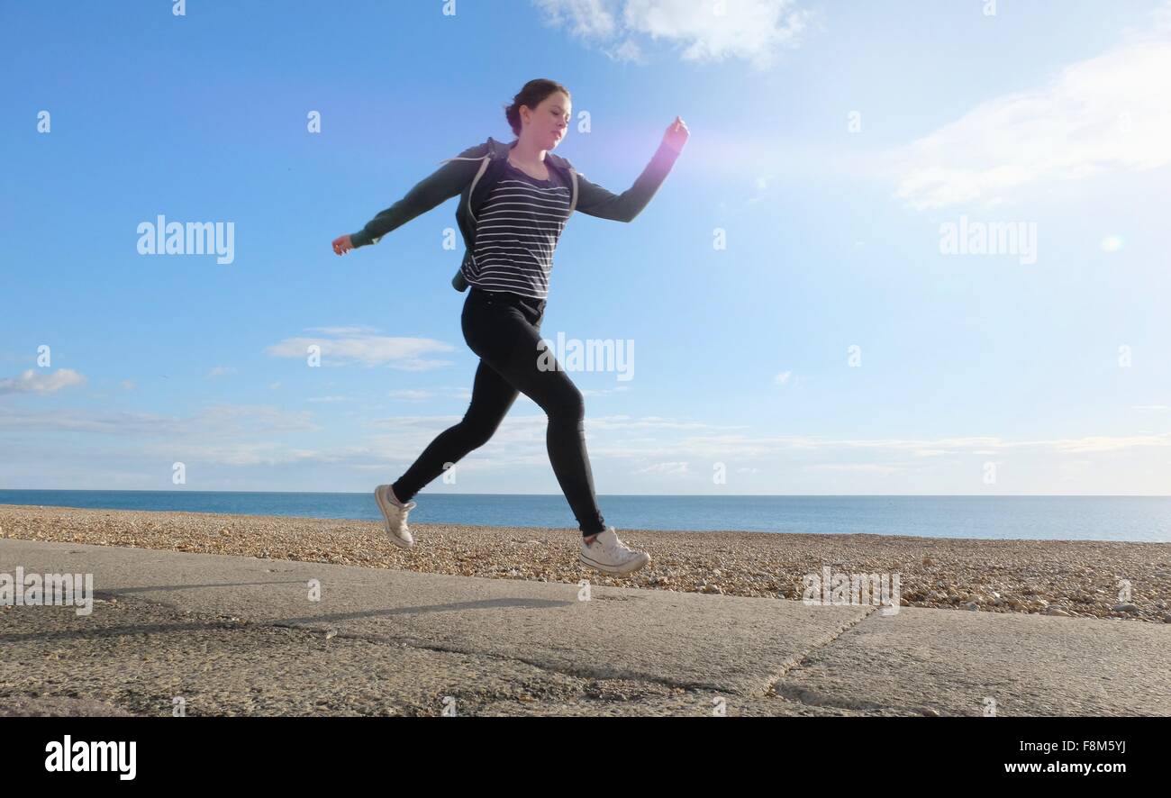 Young woman running along path on shingle beach Stock Photo
