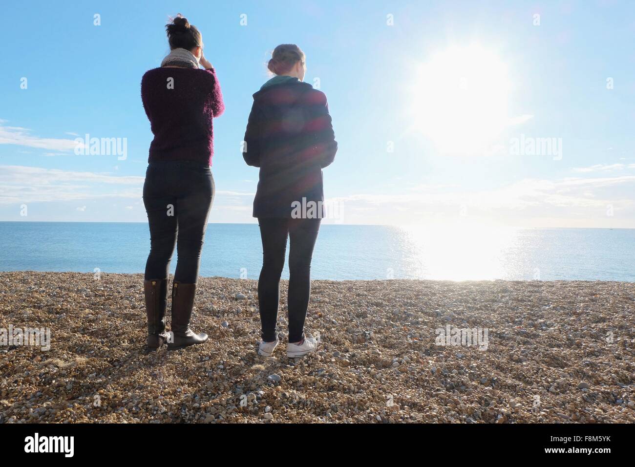 Rear view of two young adult sisters looking out at sunlit sea Stock Photo