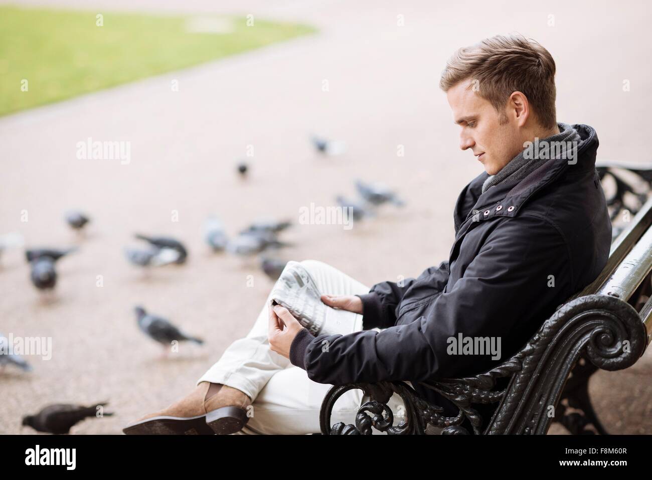 Young man sitting on park bench reading newspaper Stock Photo - Alamy