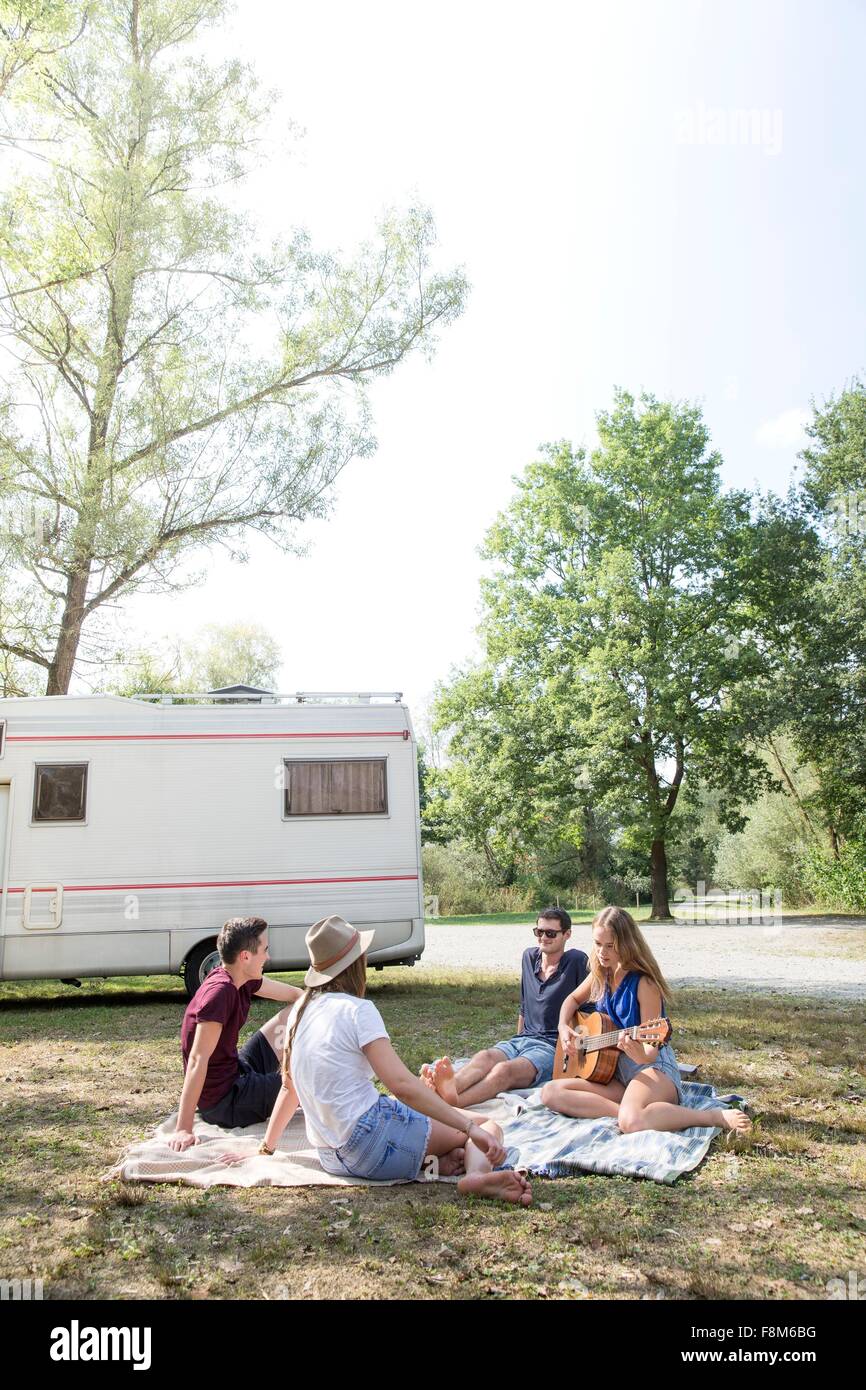 Group of young adults sitting on picnic blanket , relaxing, camper van in background Stock Photo