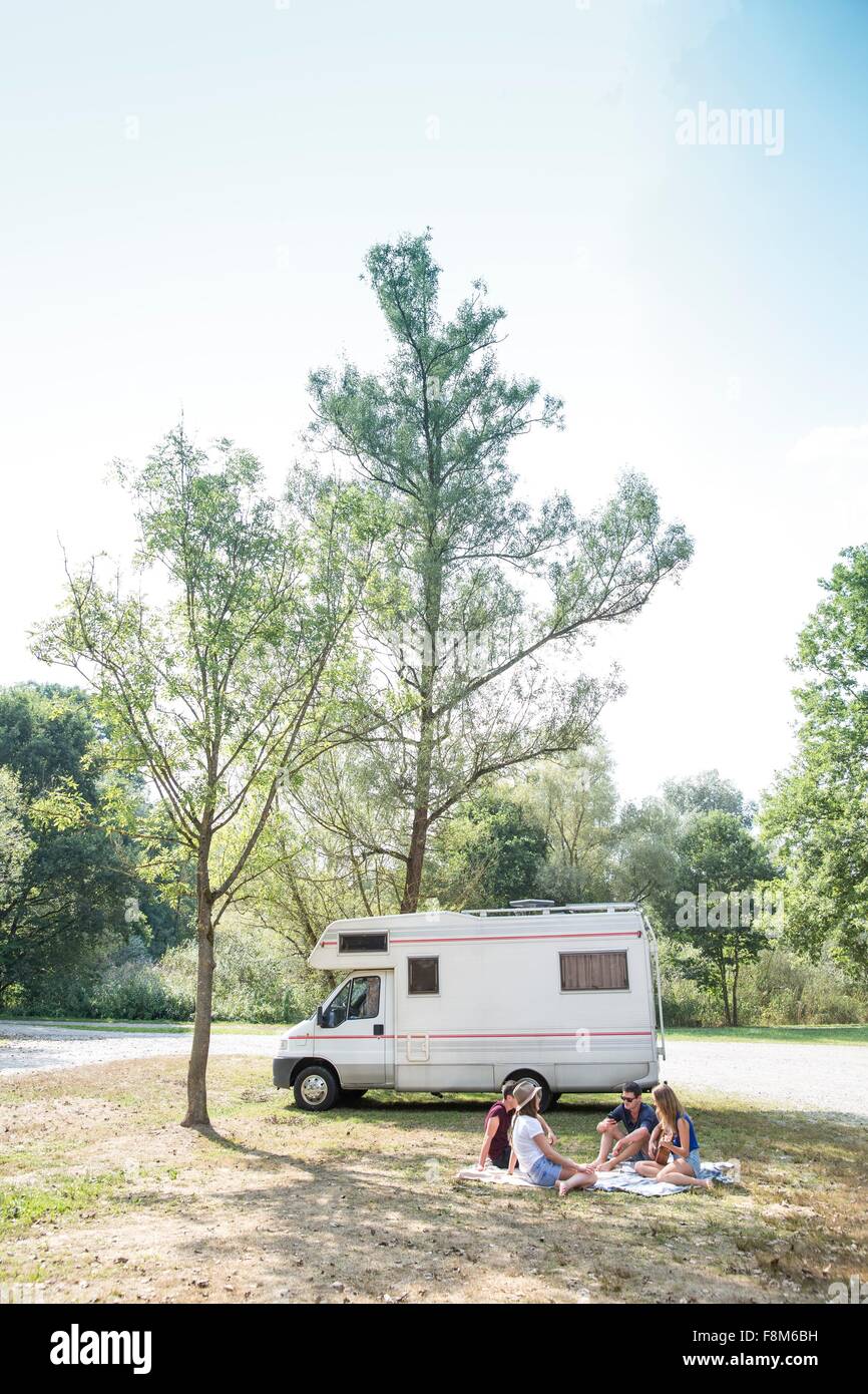 Group of young adults sitting on picnic blanket , relaxing, camper van in background Stock Photo