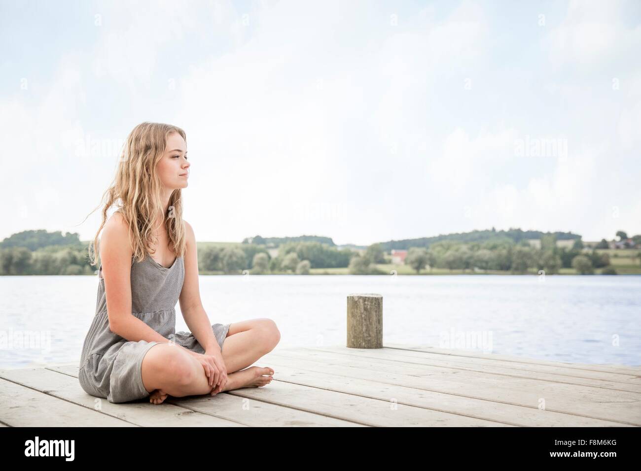 Portrait of young woman sitting on jetty, crossed legs Stock Photo