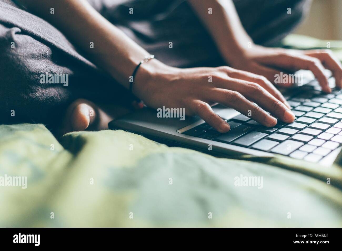 Cropped view of mid adult woman sitting cross legged on bed typing on laptop computer Stock Photo