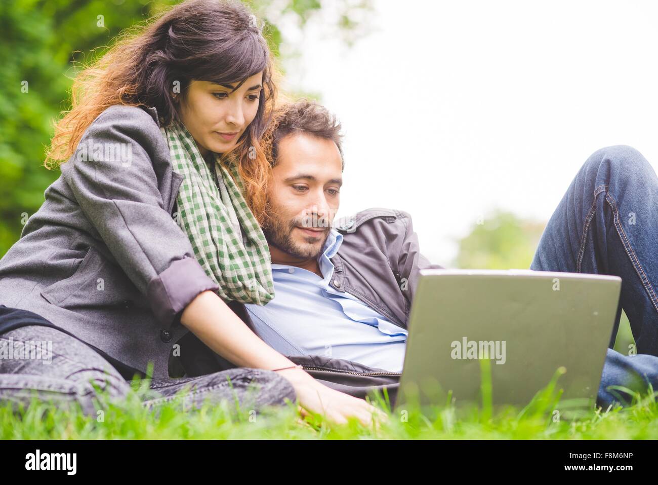 Young couple sitting on grass looking down using laptop computer Stock ...