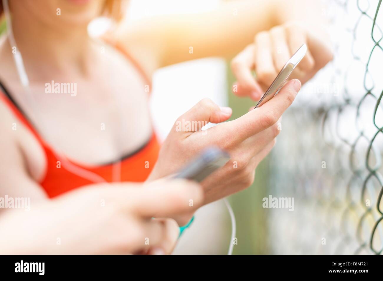 Young women using smartphone beside fence Stock Photo