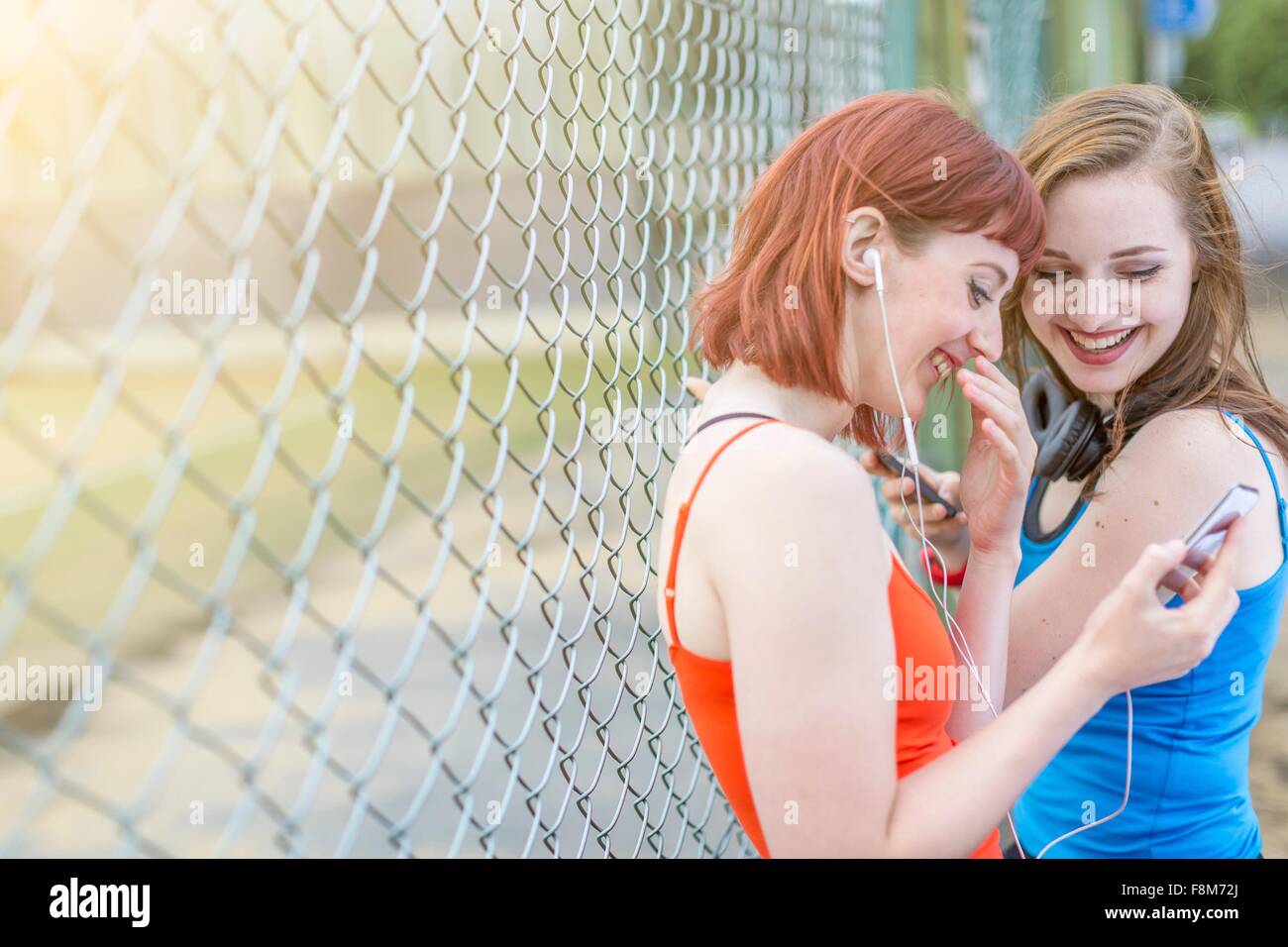 Young women using smartphone beside fence, London, UK Stock Photo