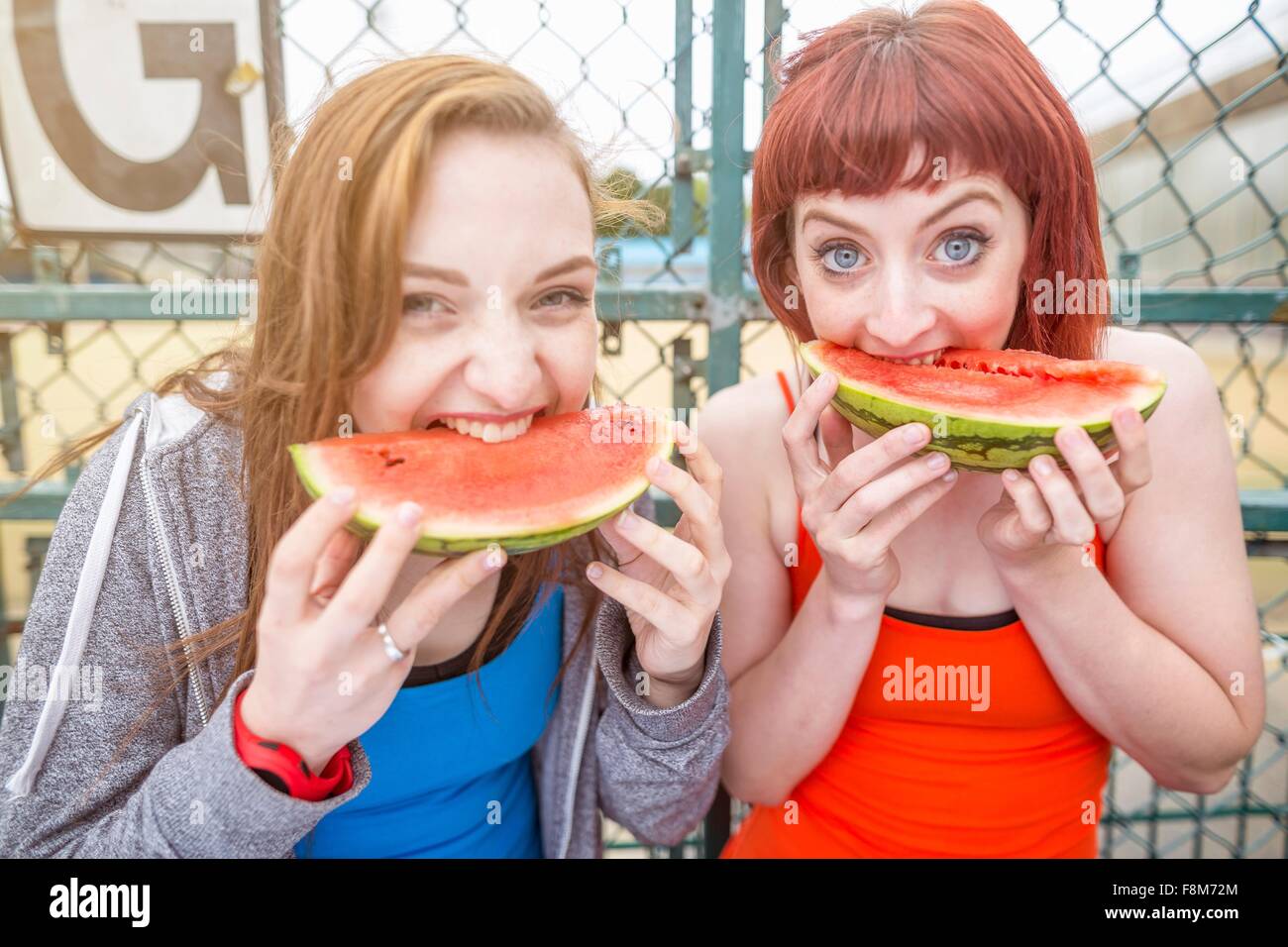 Young women eating watermelon beside sports ground, London, UK Stock Photo
