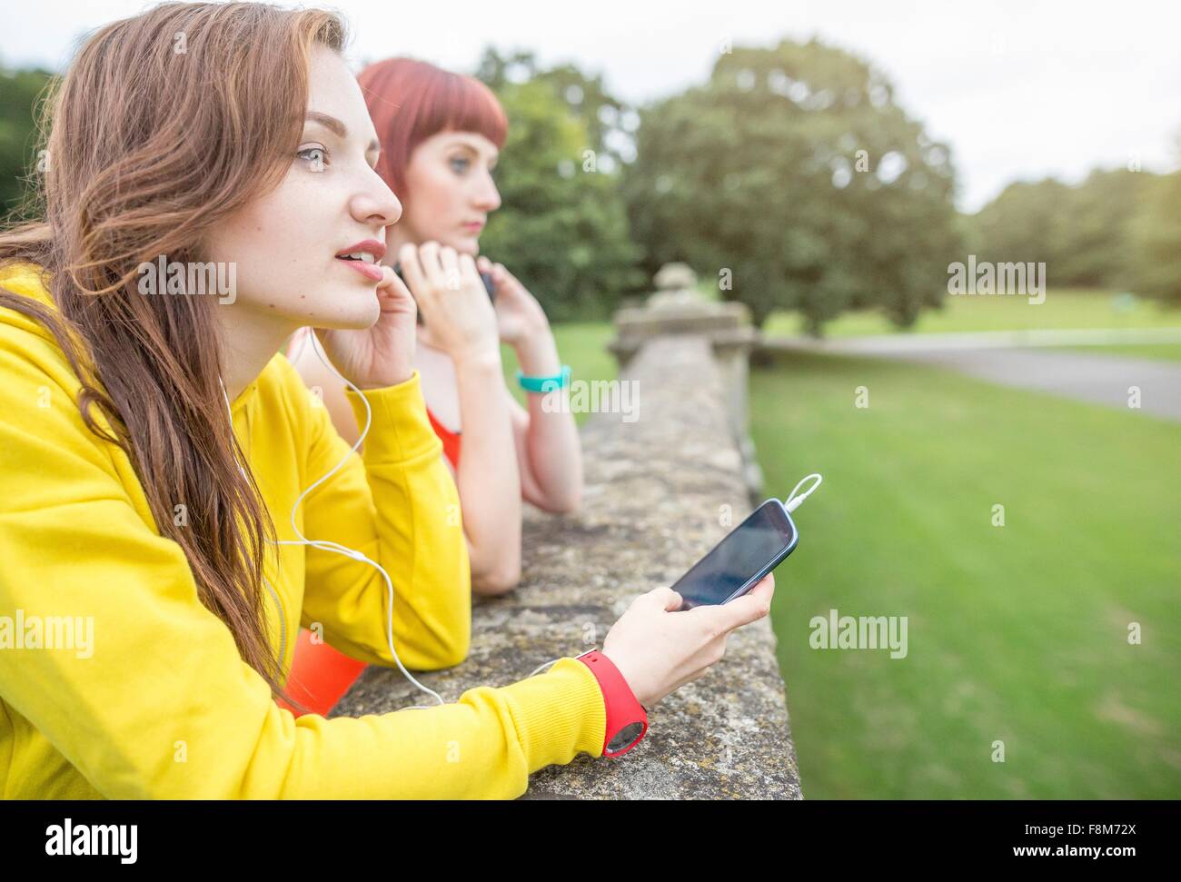 Young woman with smartphone leaning against stone wall Stock Photo