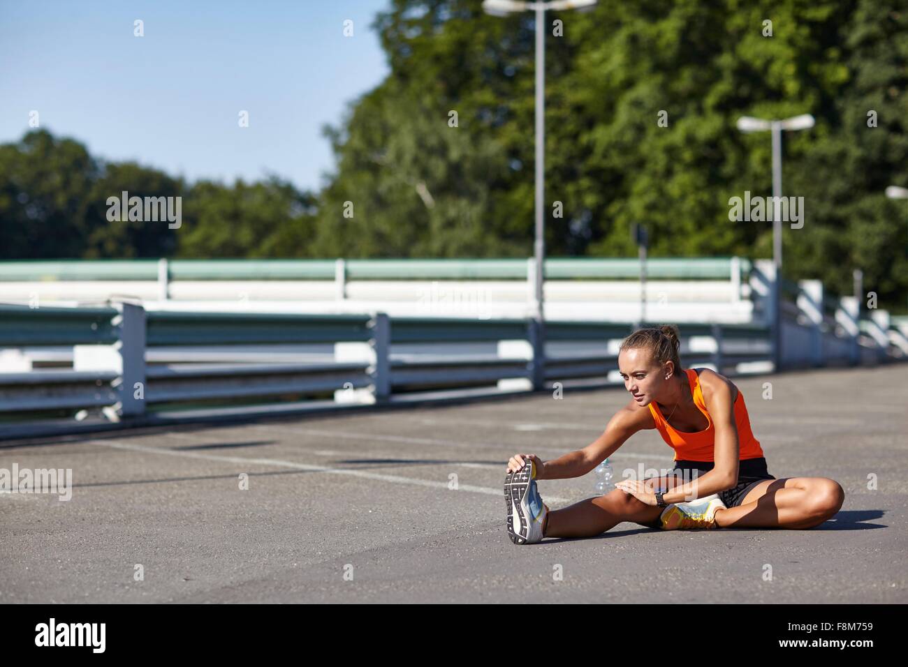 Young female runner touching toes in parking lot Stock Photo