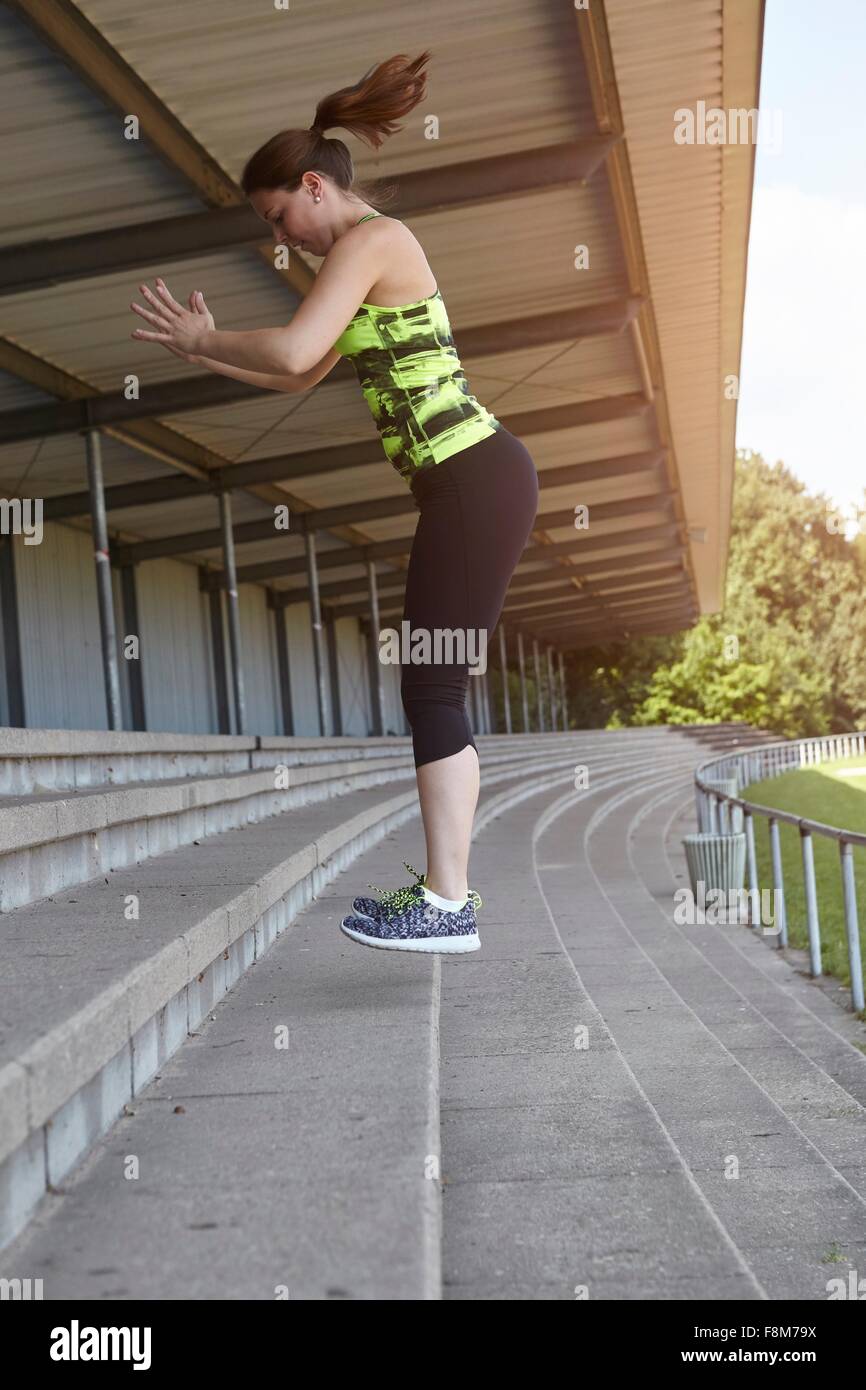 Young female runner doing training jumps in stadium seating Stock Photo