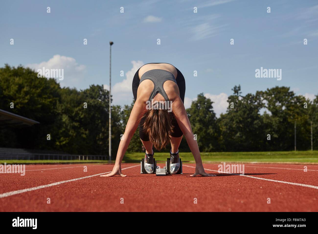 Young female runner bending forward on race track starting line Stock Photo