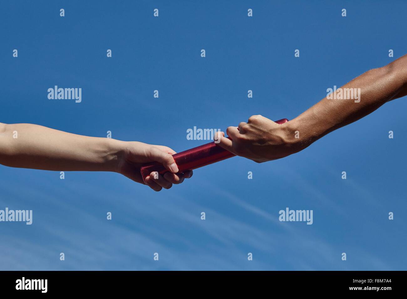 Hands of female relay runners passing baton against blue sky Stock Photo