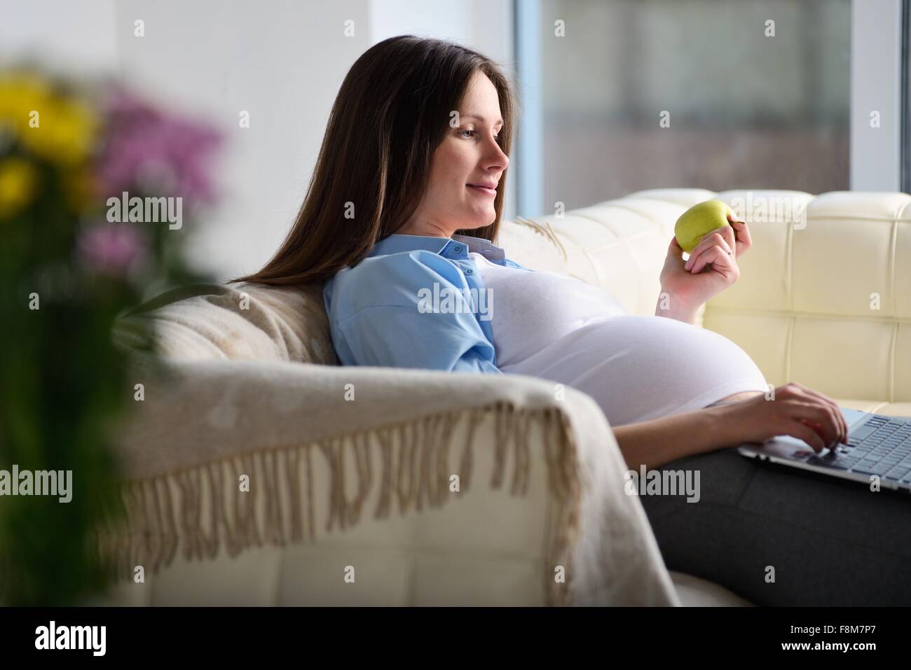 Pregnant woman sitting on sofa, using laptop Stock Photo