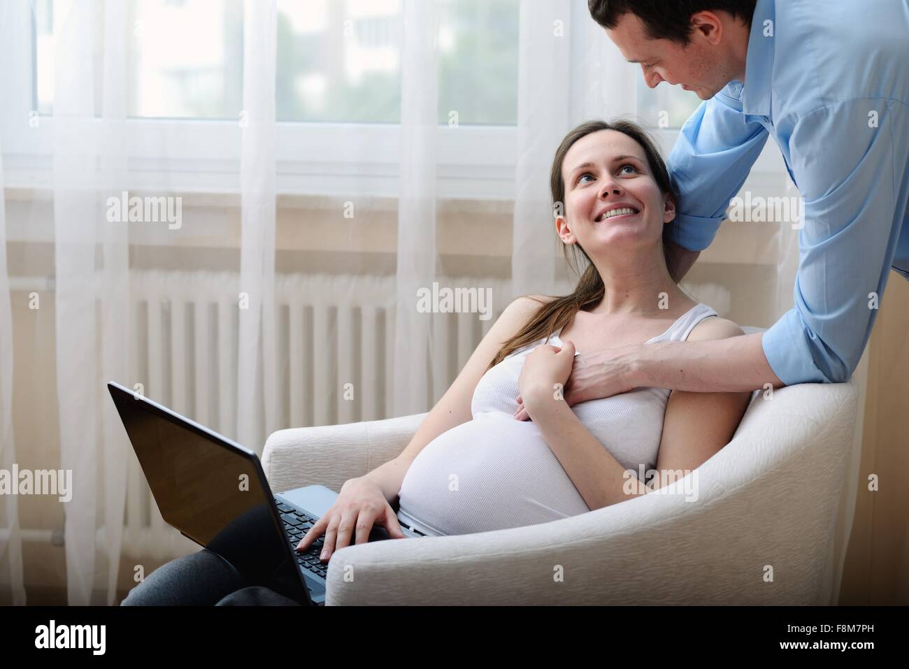 Pregnant woman sitting in chair, using laptop, husband holding her hand Stock Photo