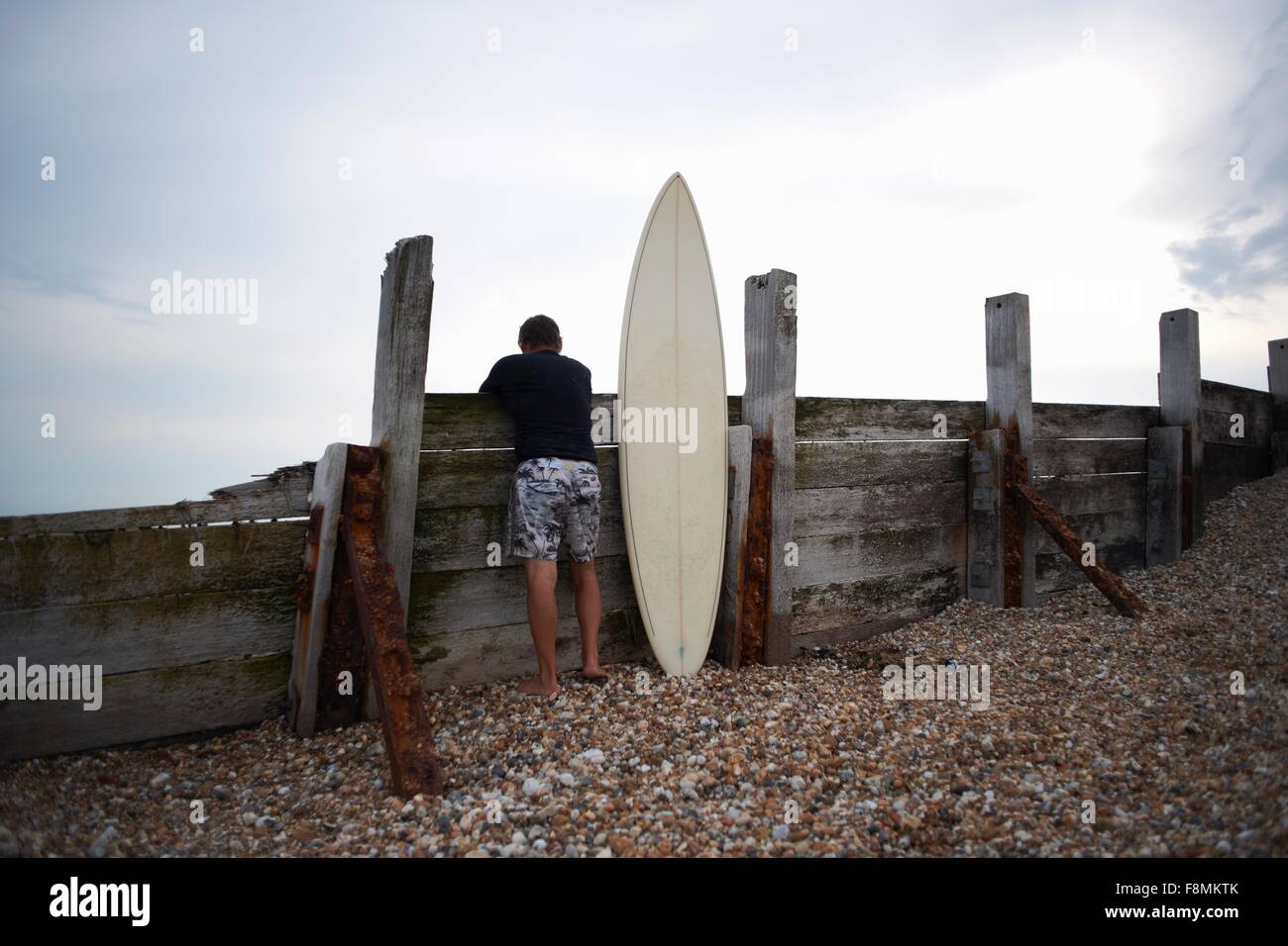 Surfer leaning against wooden fence with surfboard Stock Photo - Alamy