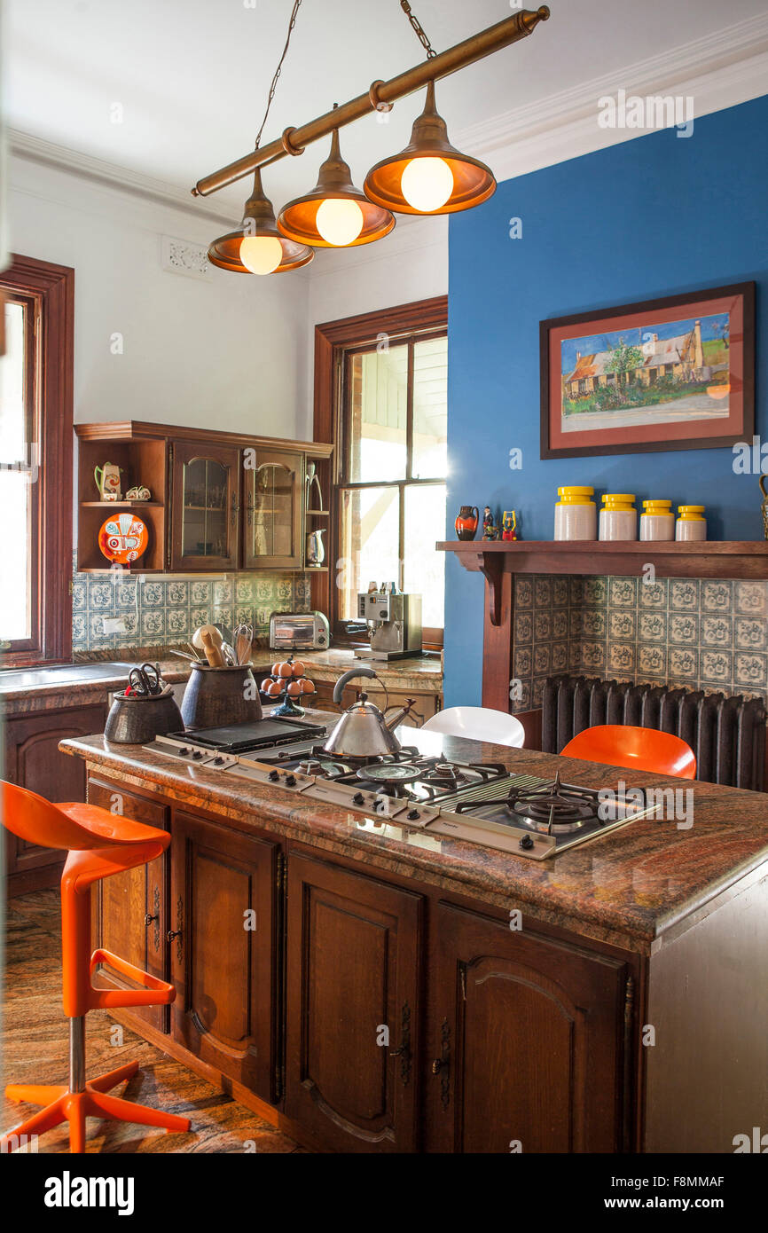 The home of designer Erica Pols. The kitchen with blue feature wall. Shelves and an island with cupboards and bright orange Alessi stools. Traditional style kitchen units with wooden doors. Stock Photo