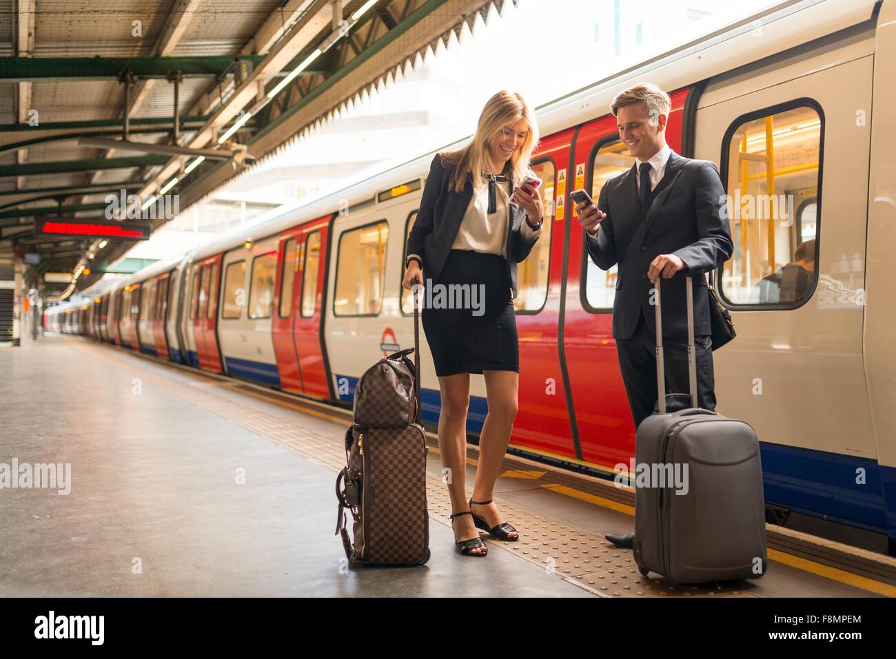 Businessman and businesswoman texting on platform, Underground station, London, UK Stock Photo
