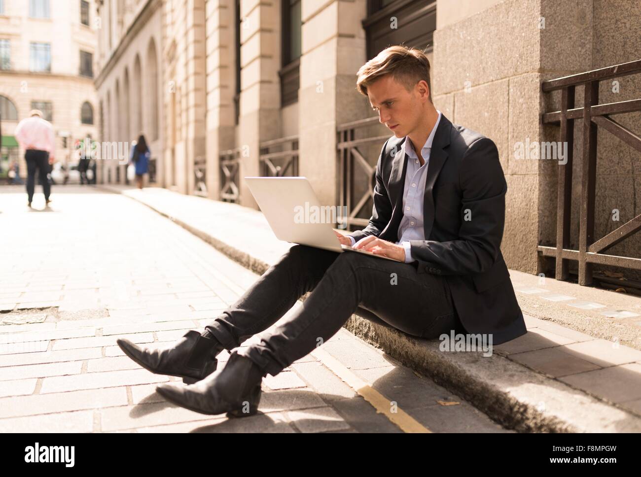 Businessman using laptop on kerb, London, UK Stock Photo