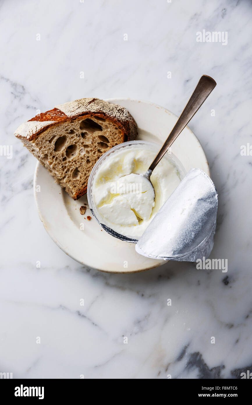 Clabber sour milk in plastic box with foil cap and brown rye bread on white marble background Stock Photo