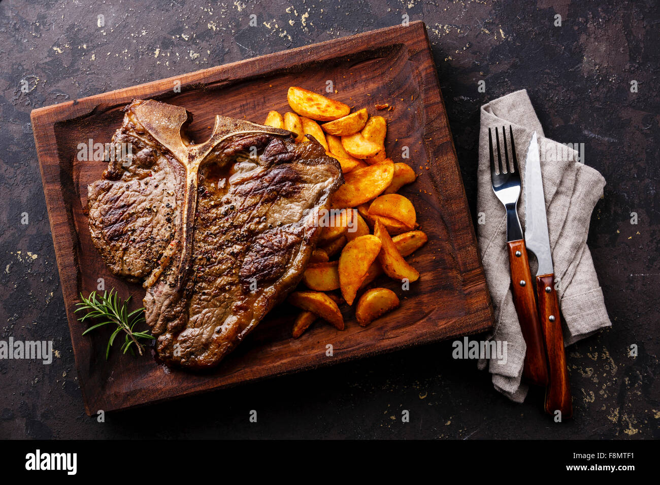 Medium rare Grilled TBone Steak with potato wedges on serving board block on dark background