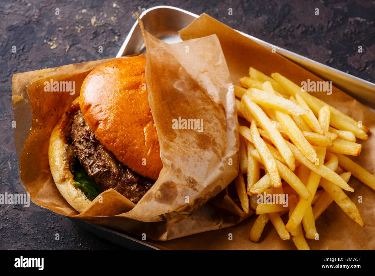 Burger with meat and French fries in aluminum tray on dark background Stock Photo