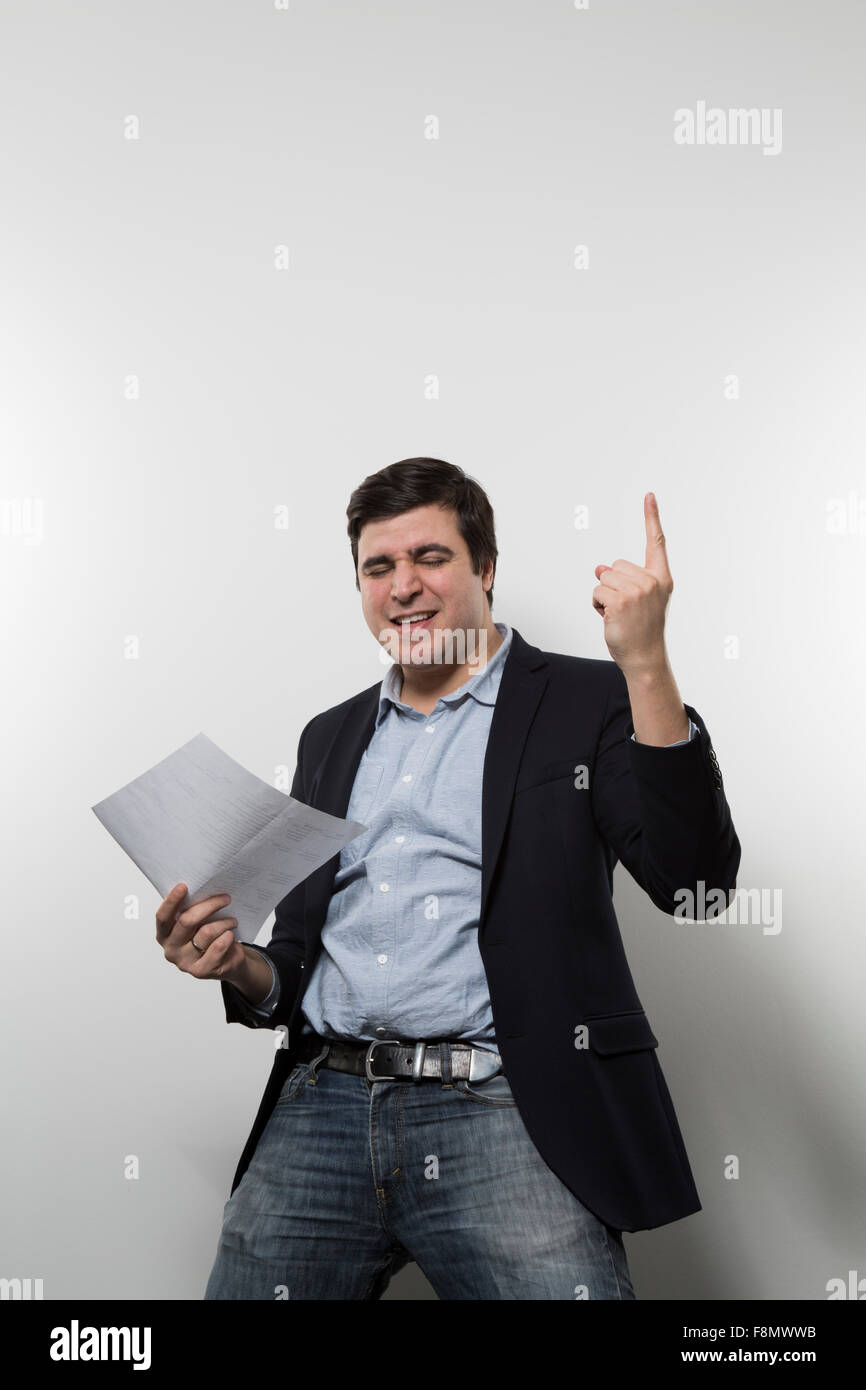 Dark-haired european businessmann is dancing full of delight with his left index finger into the air and a piece of paper in his Stock Photo
