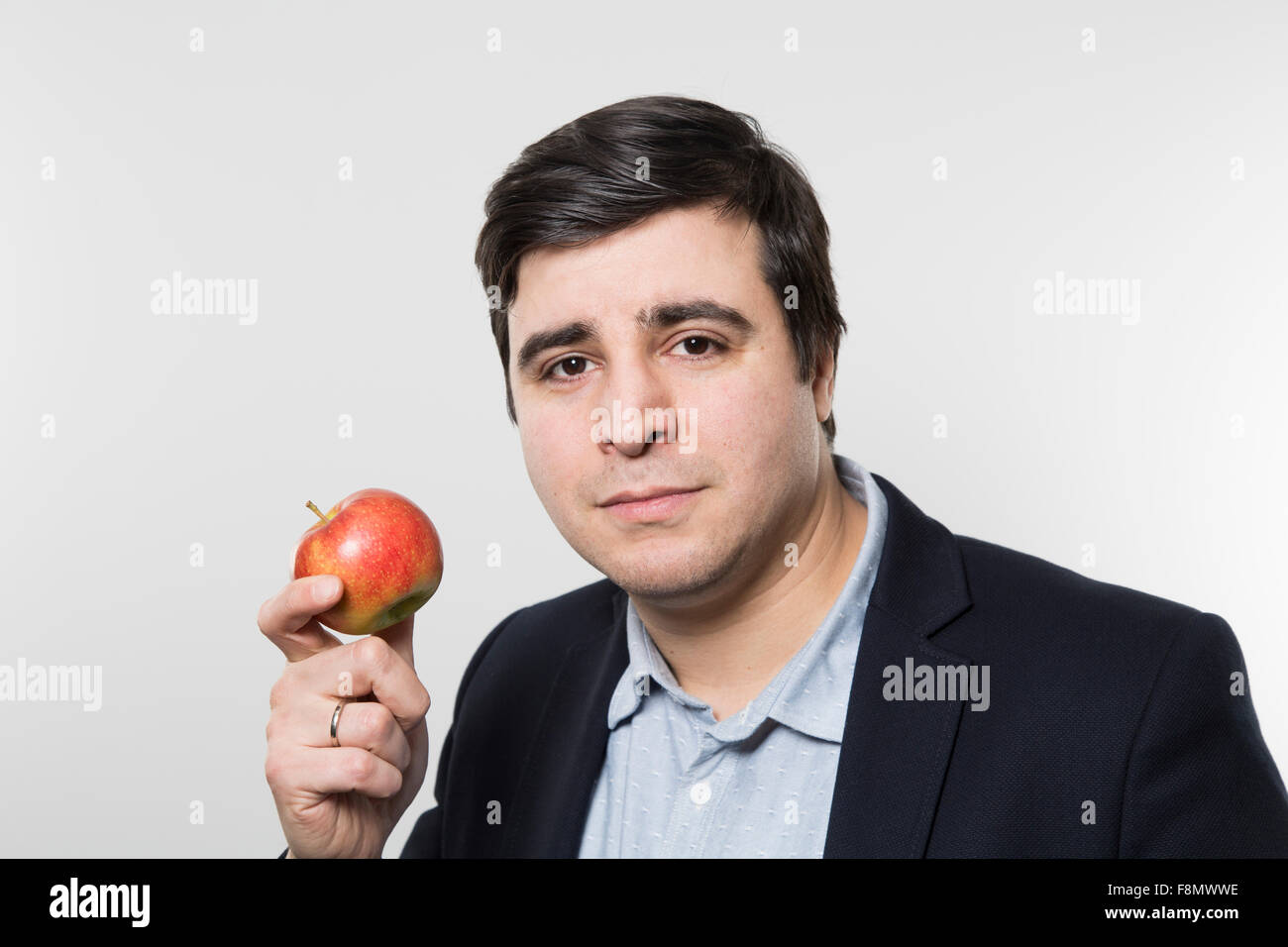 Dark-haired european businesmann with a trusting look hold an small apple while in front of a gradient background Stock Photo