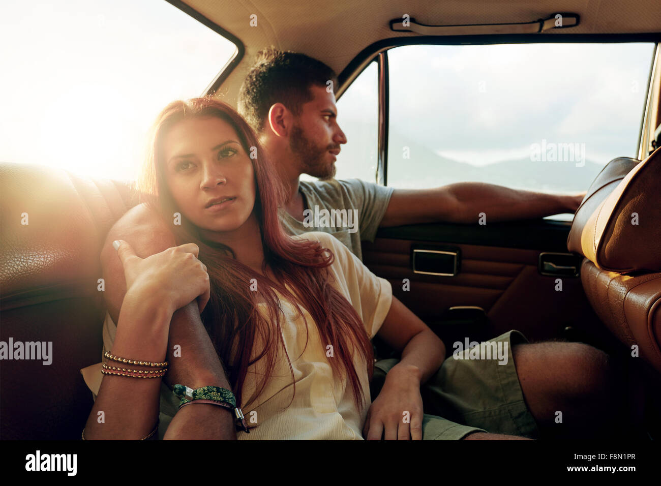 Shot of young woman with her boyfriend sitting on back seat of a car going on road trip. Couple in rear seat of vehicle. Stock Photo