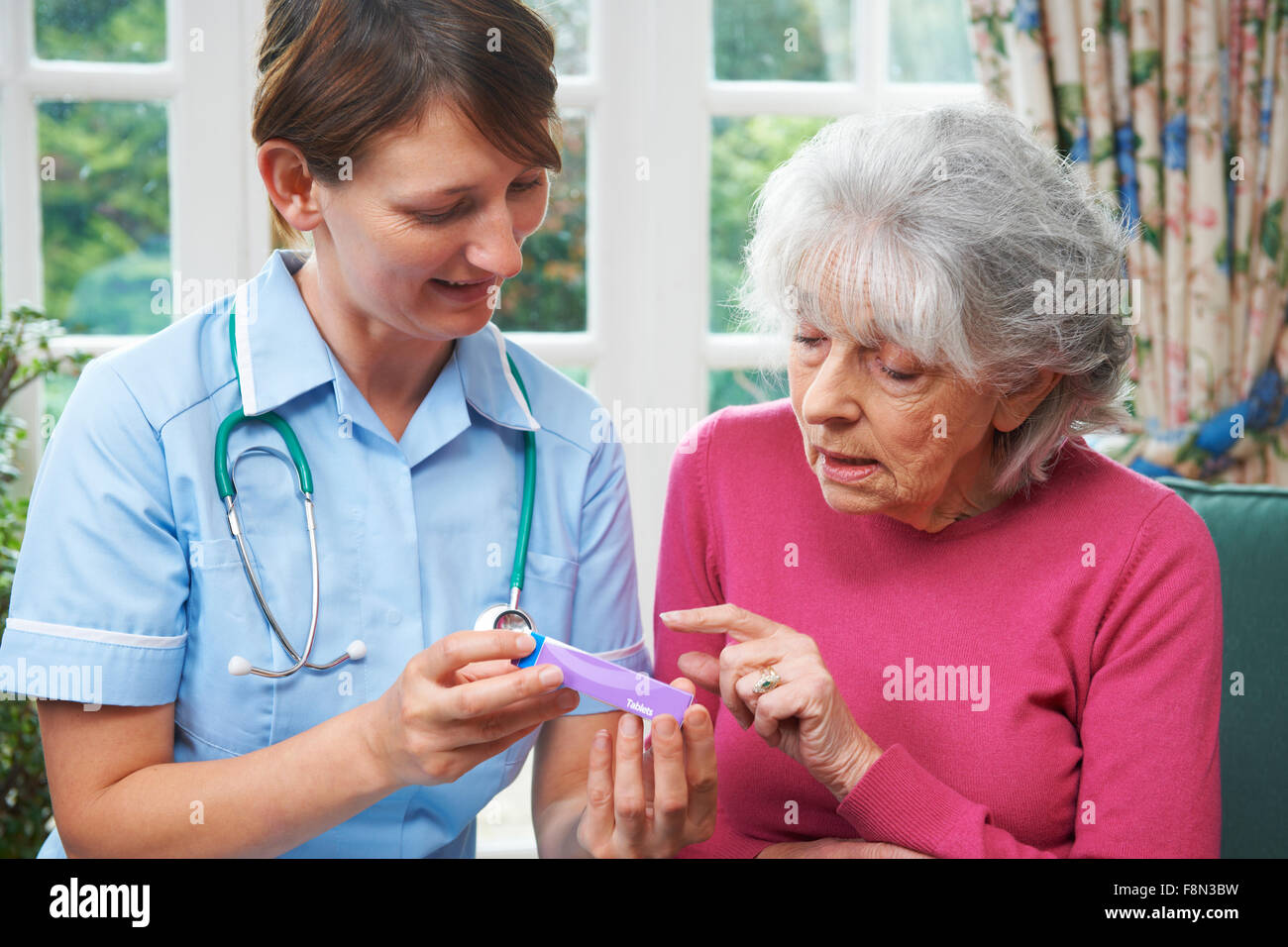 Nurse Advising Senior Woman On Medication At Home Stock Photo