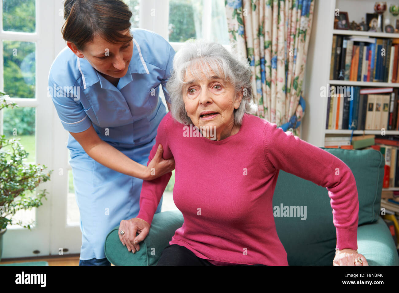 Carer Helping Senior Woman Out Of Chair Stock Photo