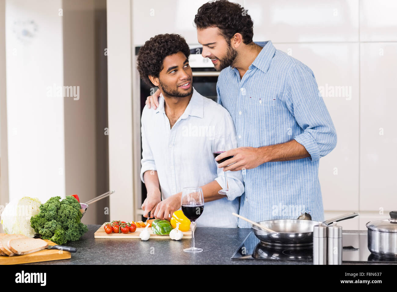 Happy gay couple drinking wine and slicing vegetables Stock Photo