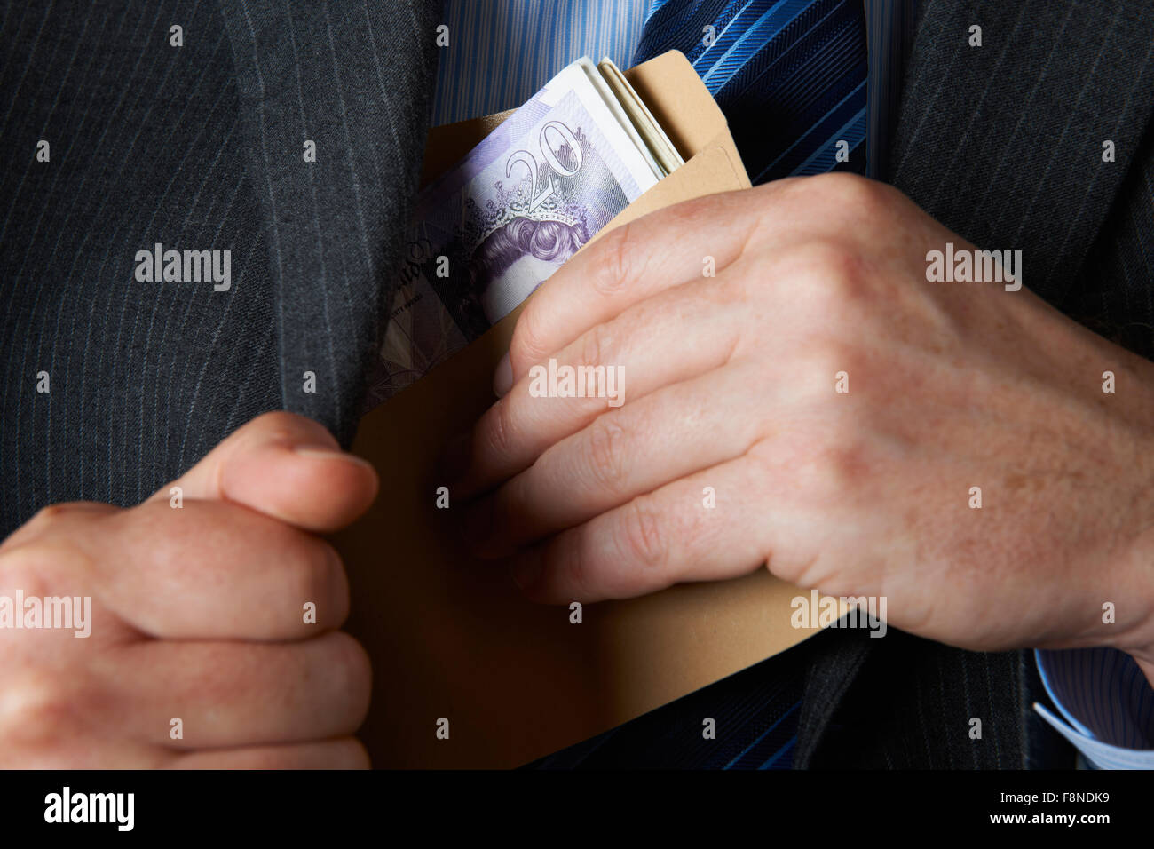Businessman Putting Envelope Filled With Sterling In Jacket Pocket Stock Photo