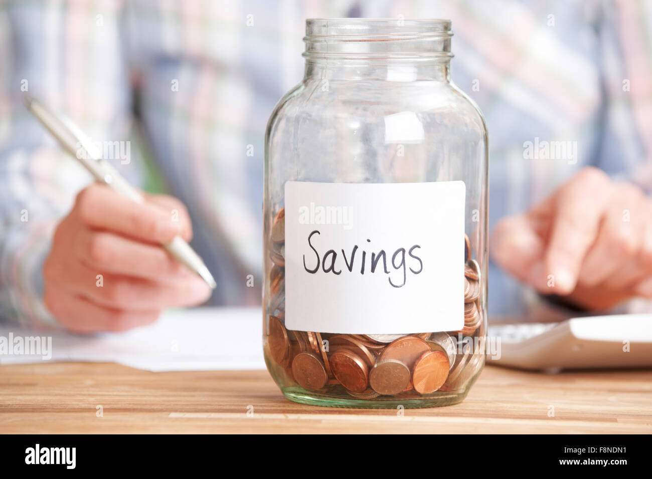 Woman Calculating Budget With Savings Jar In Foreground Stock Photo